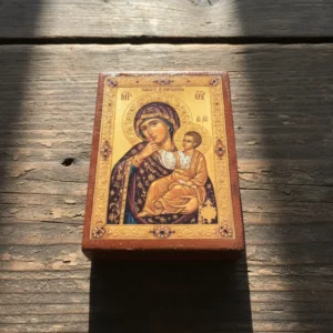 Close up of a handmade Panagia Paramythia Orthodox wooden mounted icon on a natural wood surface.